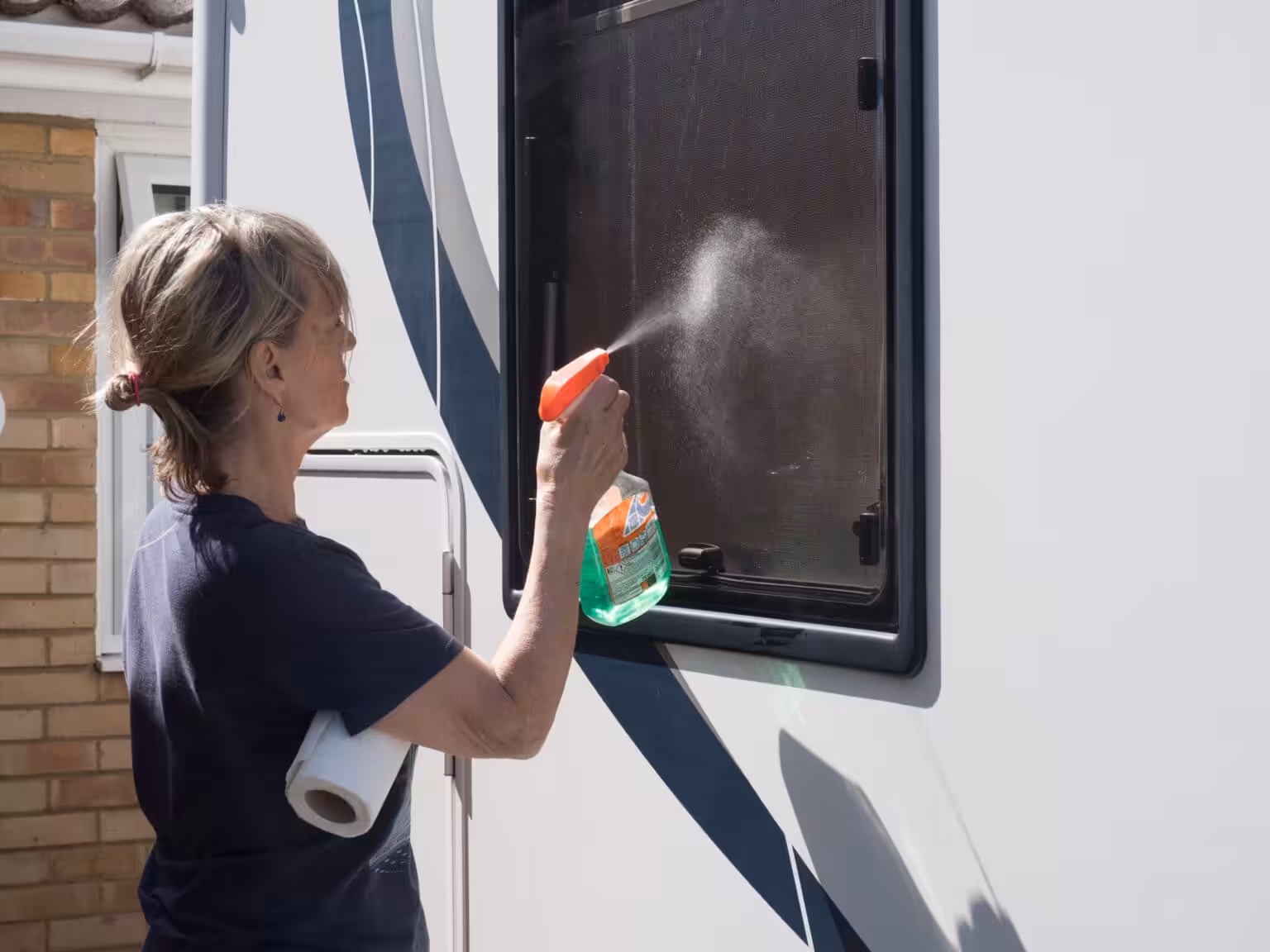 A lady motorhome owner cleans her recreational vehicle windows with green liquid spray gun.RV.
